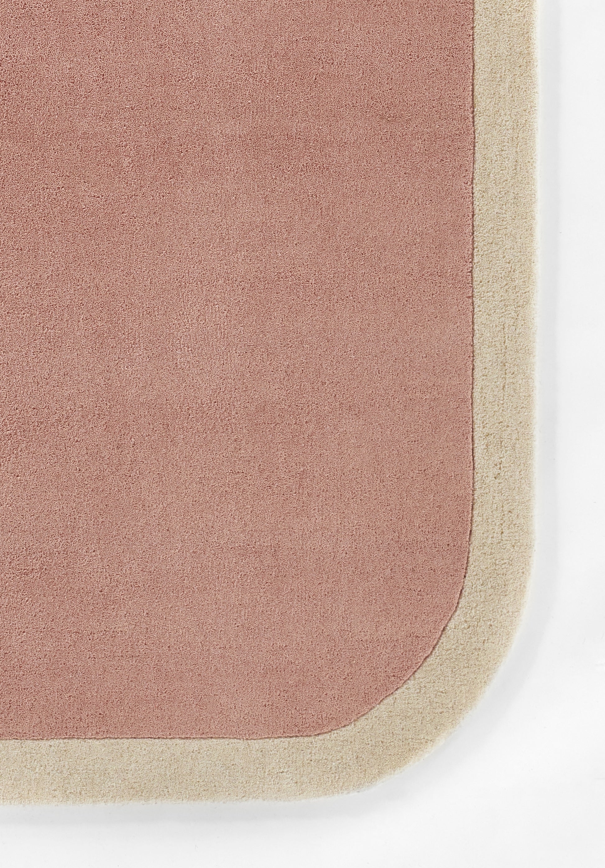 Pink rug with a cream-beige border and rounded corner; soft plush texture for indoor decor.