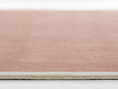 Soft pink rug with beige underside and short fringe edge; modern flat-weave style.