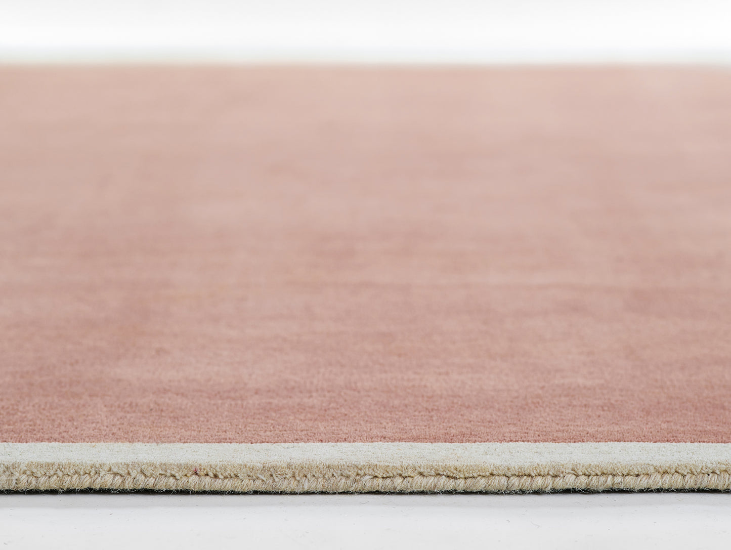 Close-up of peach-pink rug with beige underside and clean edge, modern flat-weave, soft low-pile.