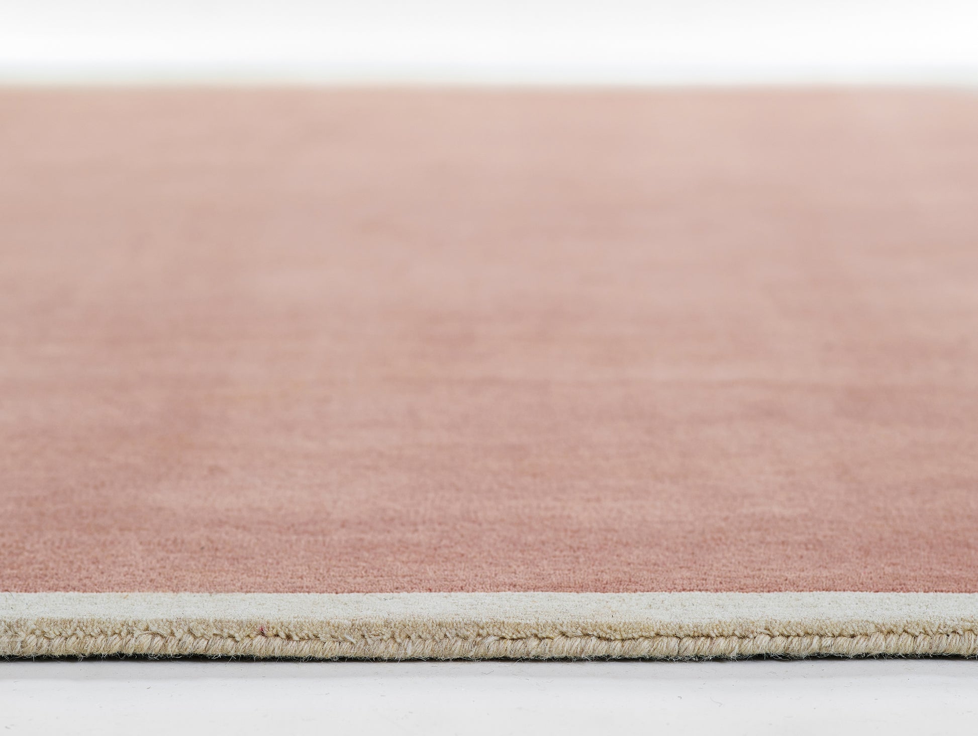 Rectangular peach-pink area rug with natural beige fringe along edge.