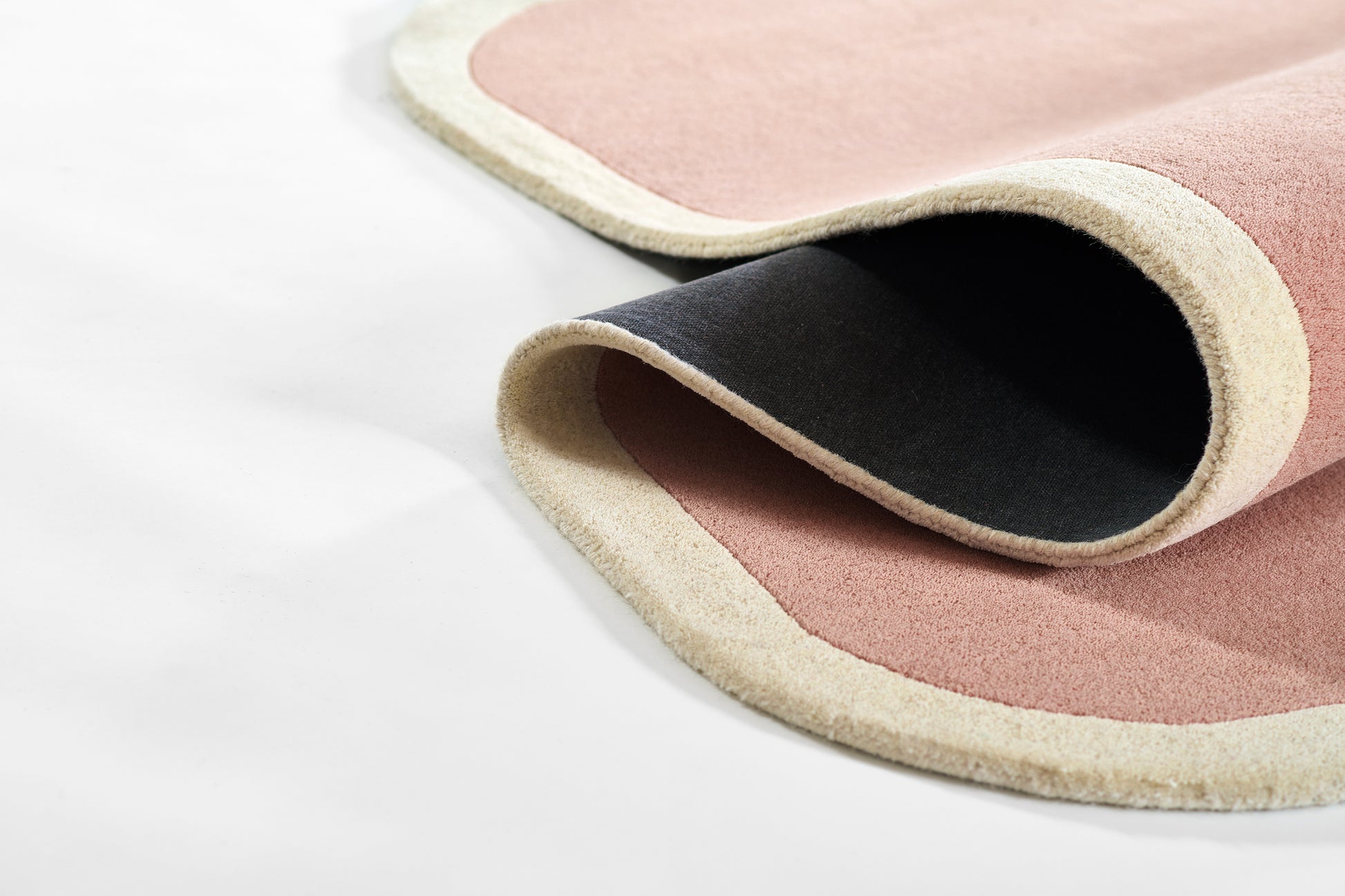 Soft pink area rug with beige border and black underside; suede-like pile, rolled edge.