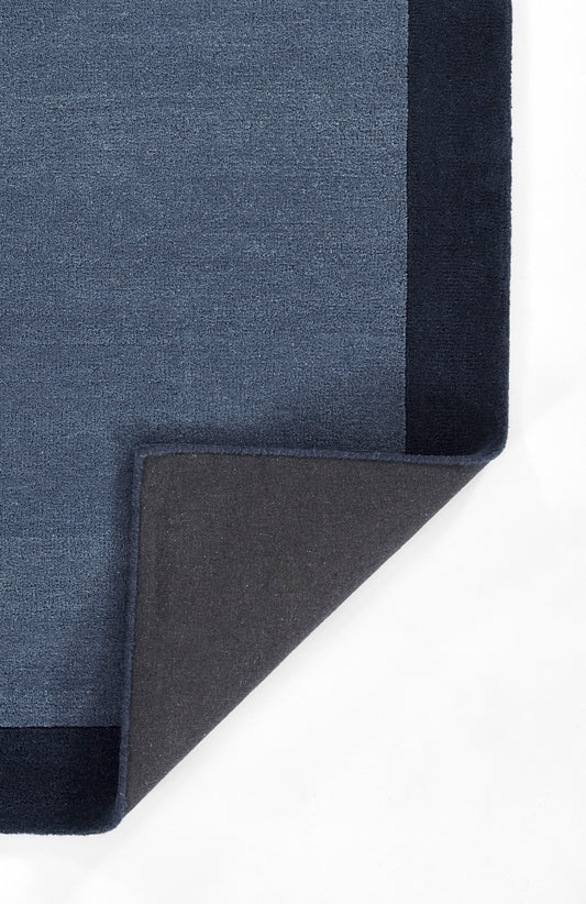 Blue textured rug with dark navy border; corner folded to reveal dark gray underside.