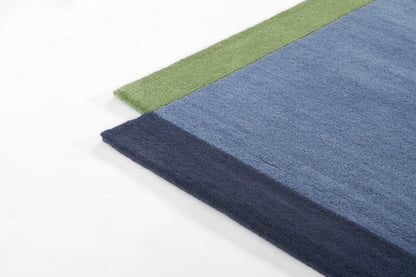 Rectangular plush rug with color-block design: green edge, light blue field, and dark navy border, soft shaggy texture.