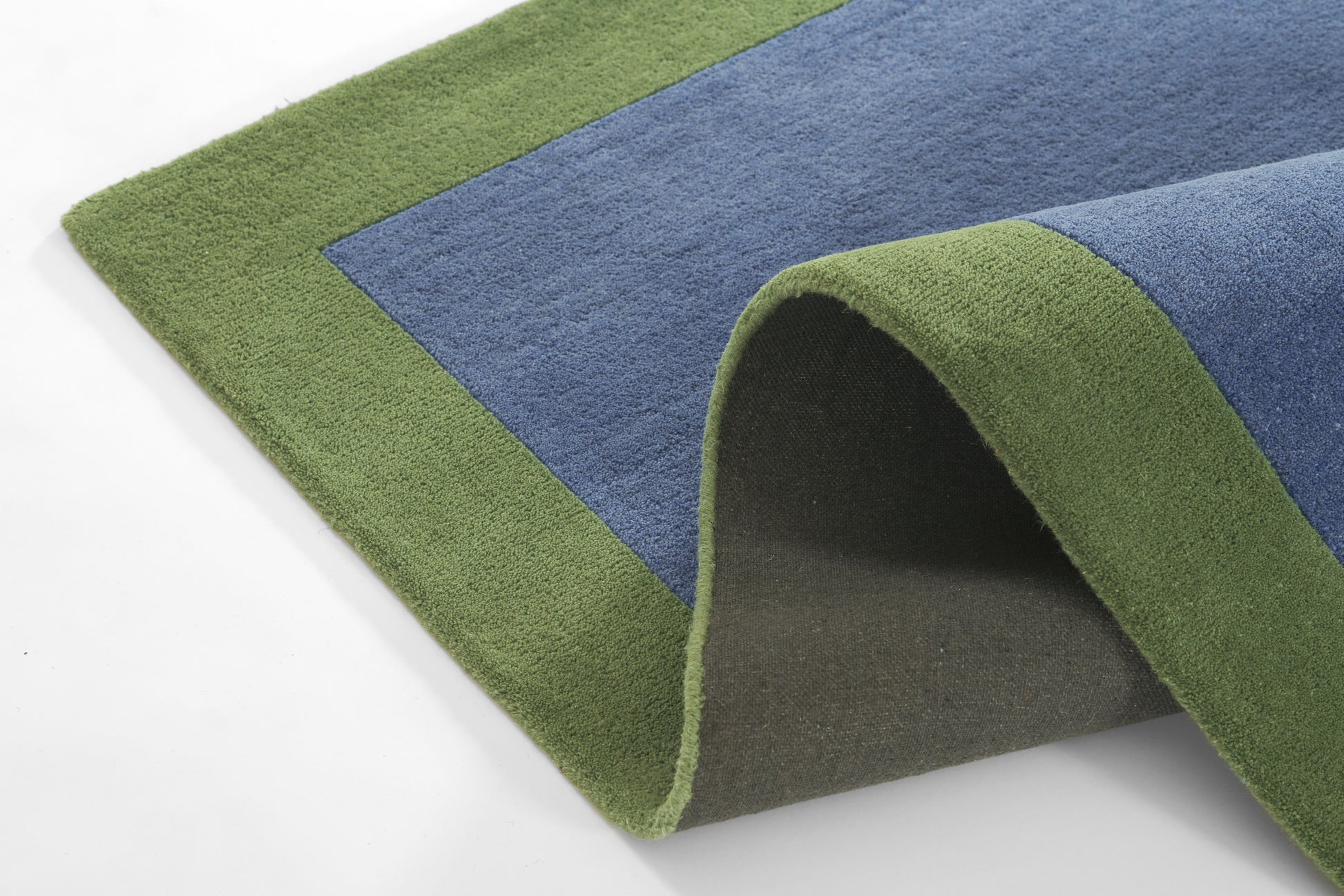 Rectangular rug with green border and blue center; plush pile, rolled corner reveals dark backing.