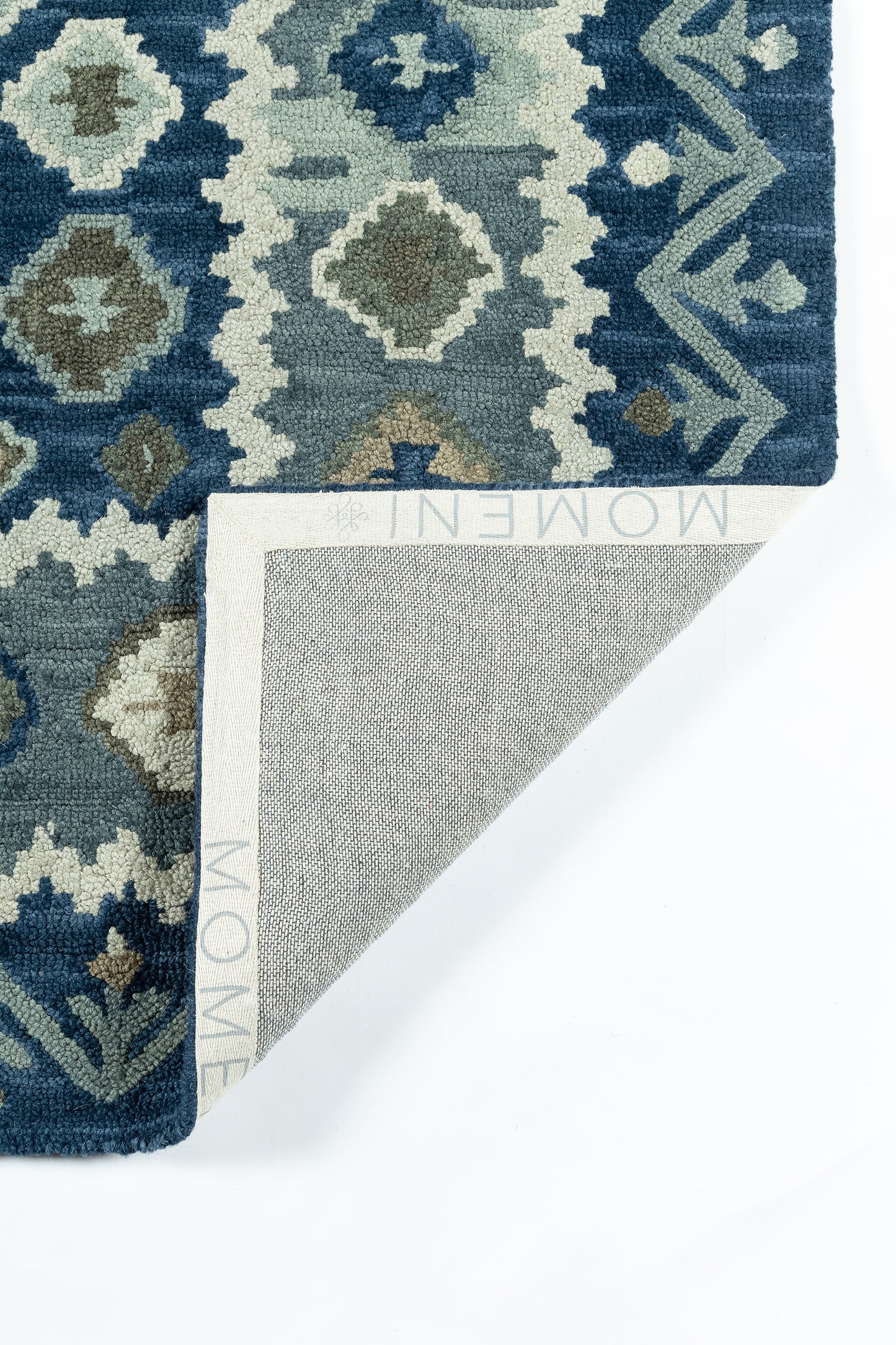 Blue geometric tufted rug with ivory, teal and brown accents; dense pile, corner folded to reveal light gray backing.