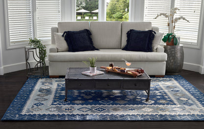 Light gray sofa with navy fringe pillows, low rectangular metal coffee table with three drawers on a blue geometric rug.