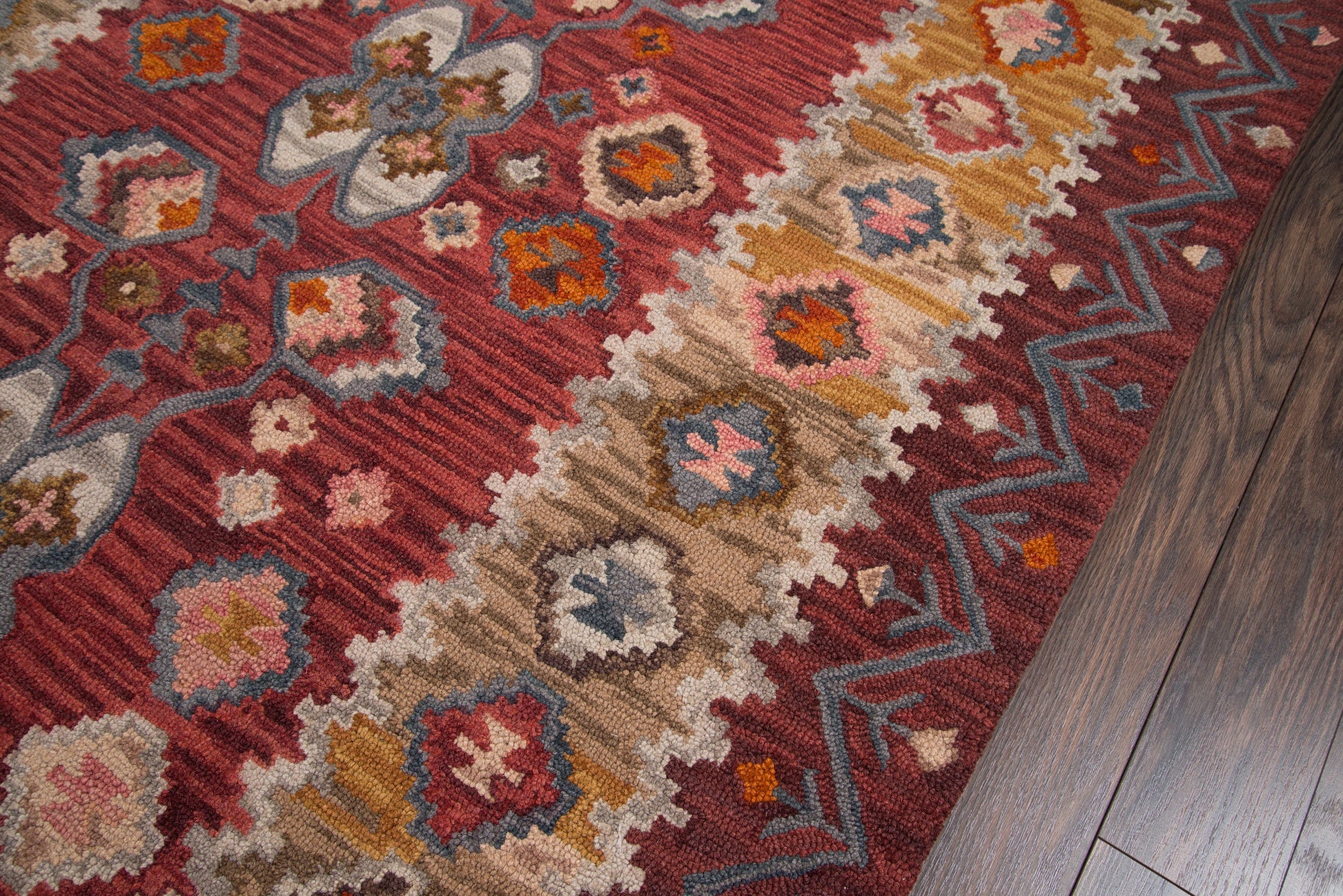 Red patterned area rug with geometric medallions in beige, blue, pink, and orange on a dark wood floor.