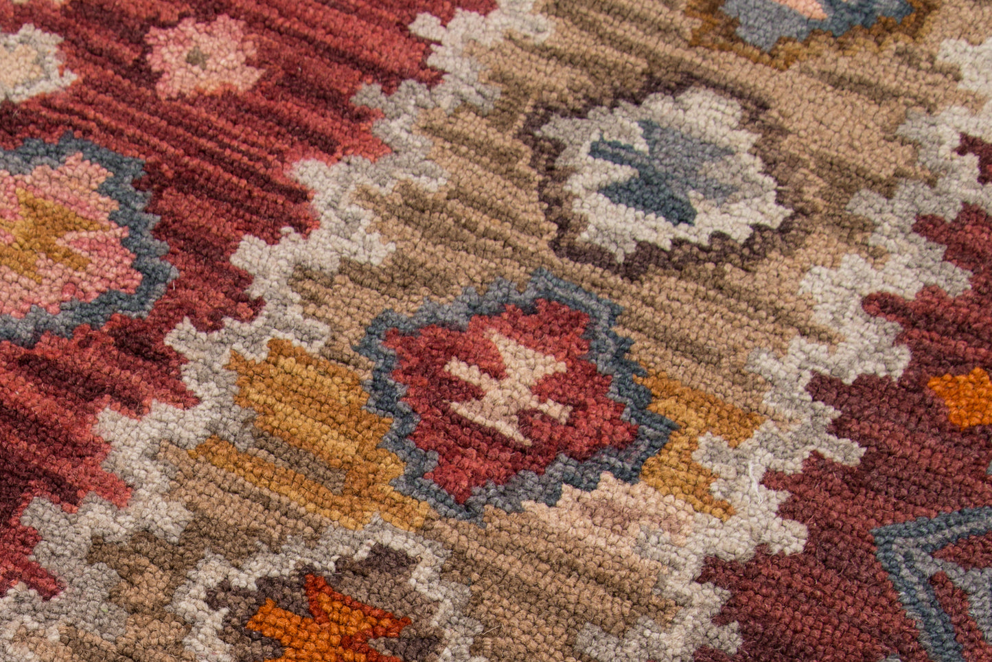Close-up of a wool oriental rug with red, tan, beige, blue and orange geometric medallions.