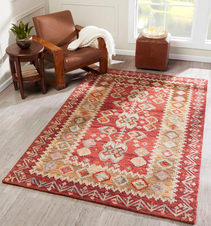 Rectangular rust-red geometric tribal area rug with beige border in a cozy seating area with a leather armchair and plant.