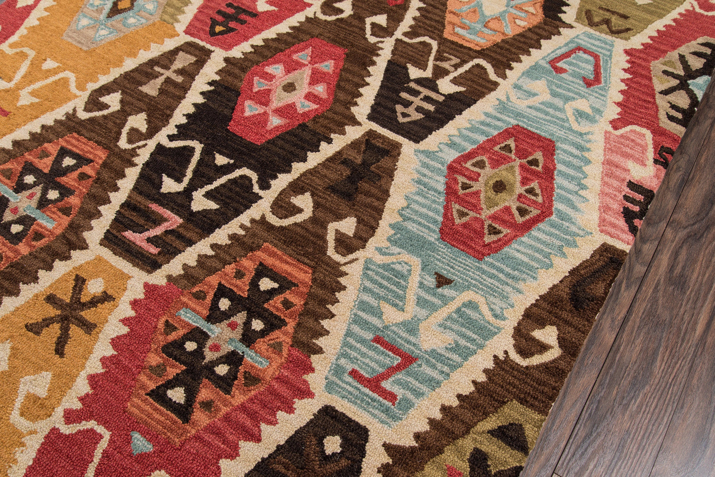 Colorful geometric tribal rug with orange, red, brown, teal and cream hues on a wooden floor.