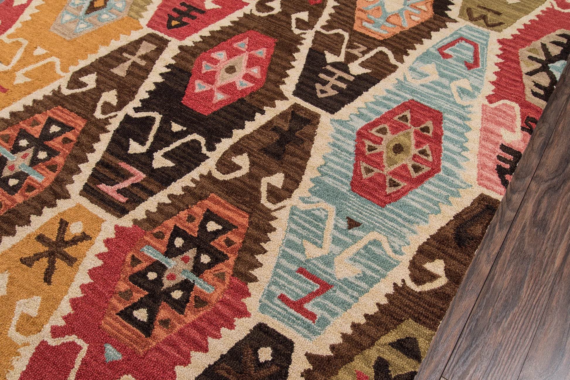 Vibrant woven kilim runner with geometric motifs in red, teal, gold & ivory on dark wooden floor.