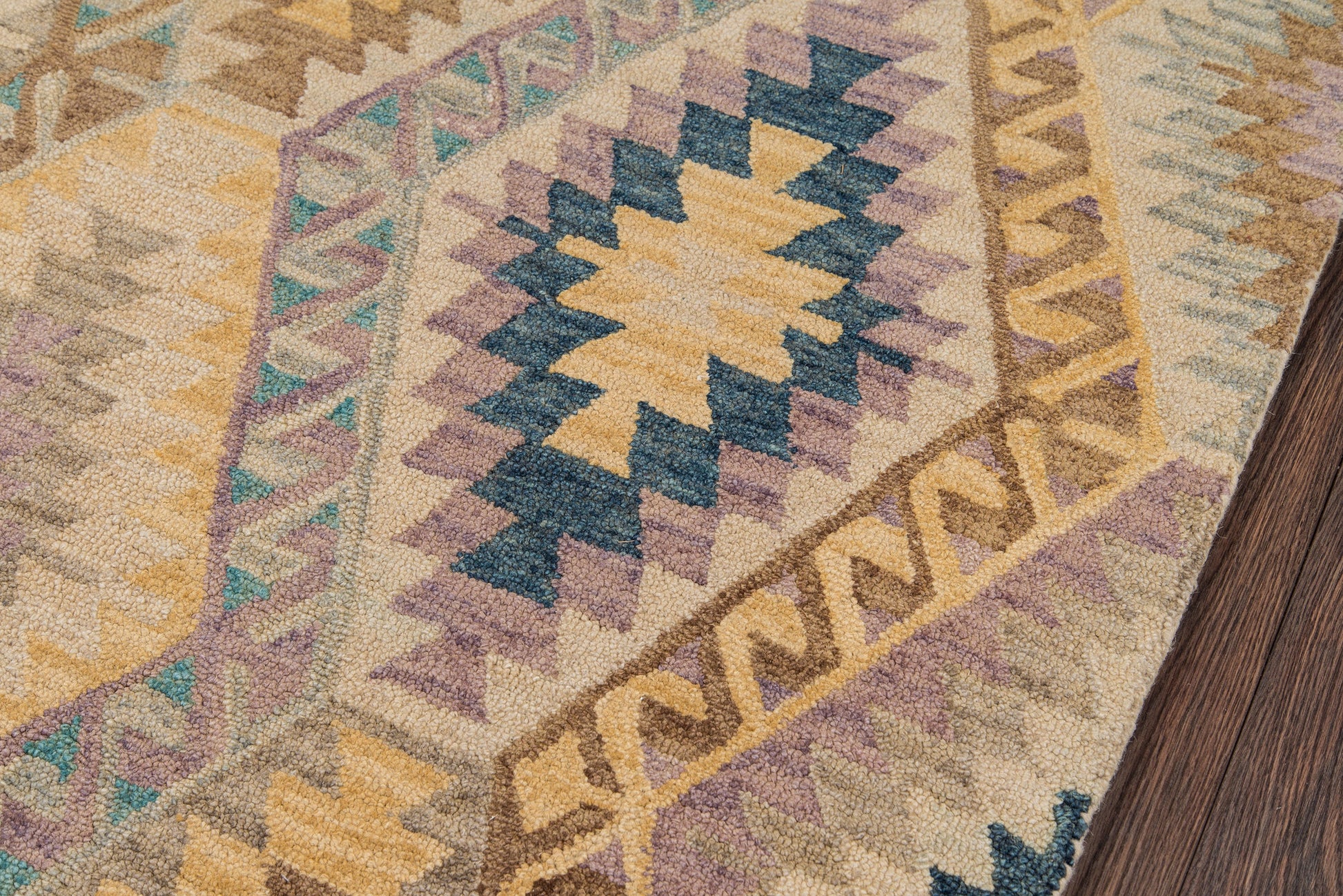 Geometric tribal area rug with zigzag diamond motifs in beige, gold, teal, purple and blue on wood floor.