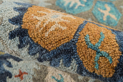Close-up of a rolled rug with orange, navy, teal and beige geometric pattern; plush tufted texture.