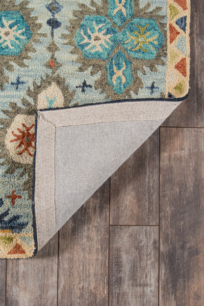Turquoise-blue ornate tufted rug with floral/medallion pattern; folded corner reveals beige backing and binding on wood floor.
