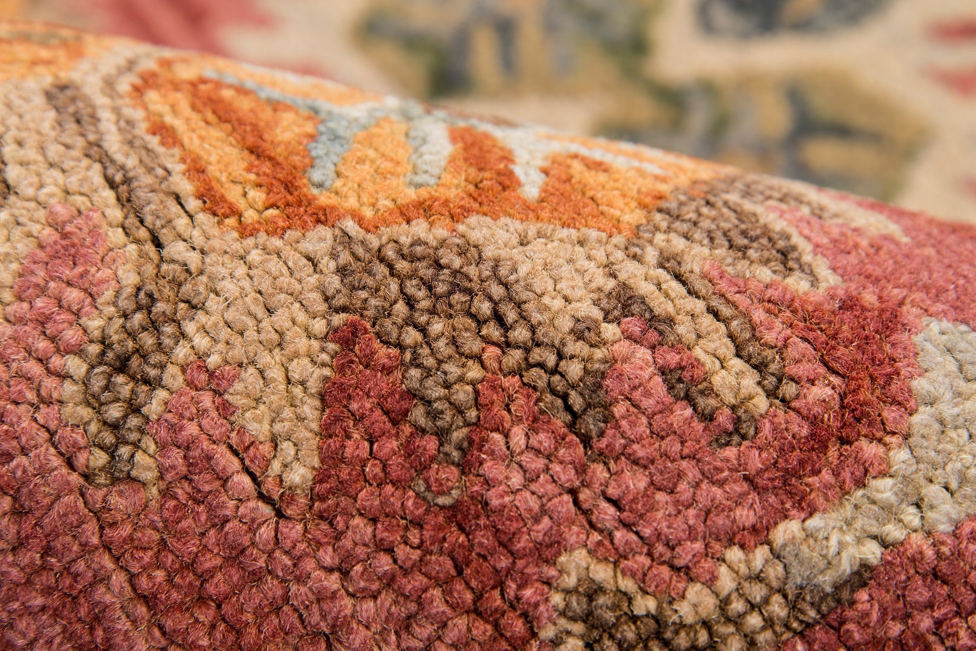 Close-up of a thick tufted wool rug with red, orange, tan and brown geometric pattern and textured pile.
