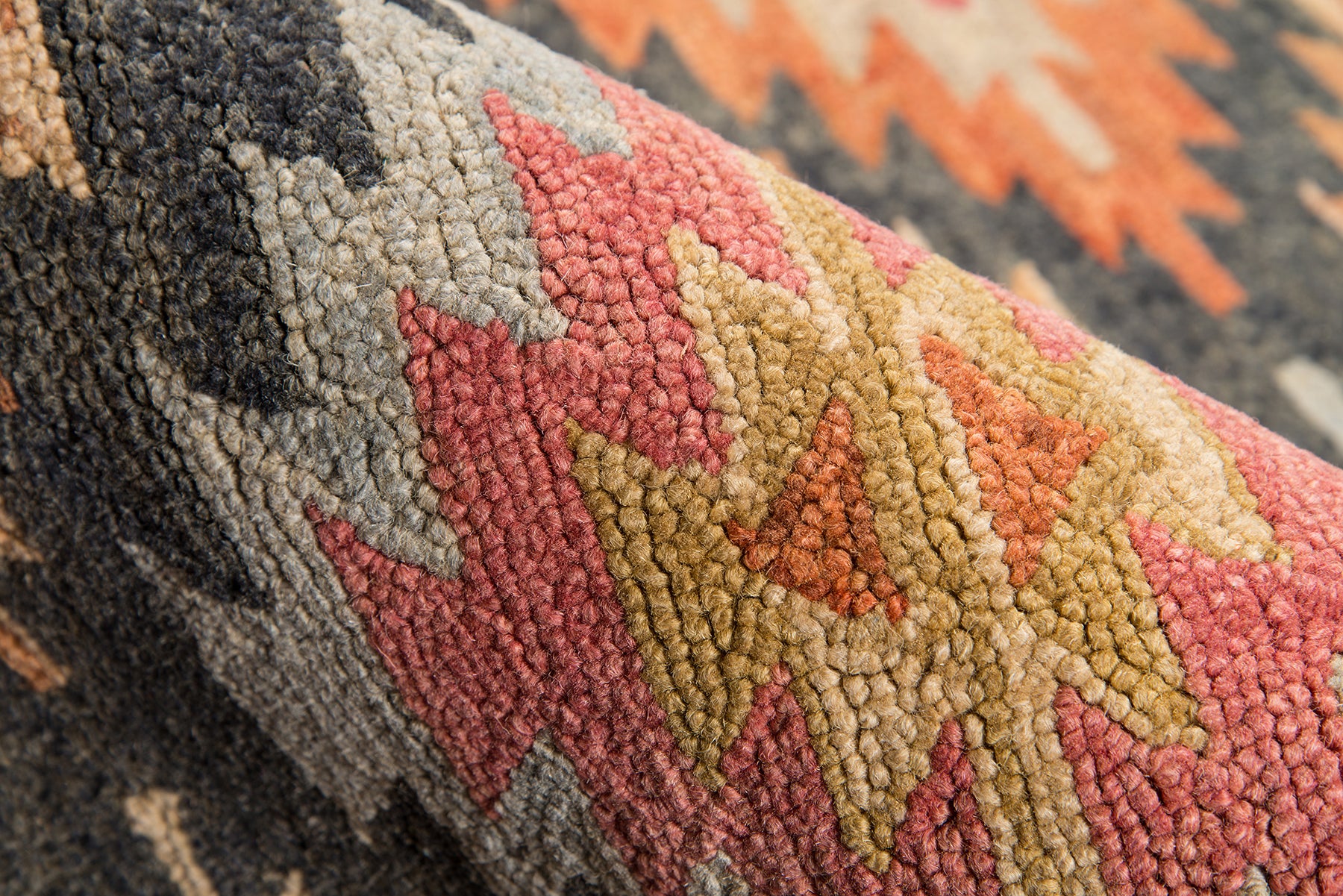 Close-up of a chunky tufted geometric tribal rug in black, gray, pink, olive, and tan with zigzag motifs.