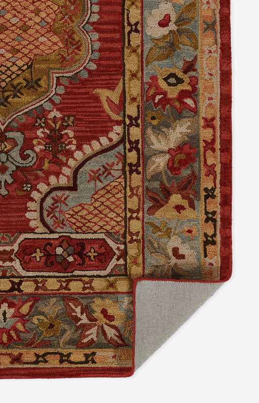 Close-up of red oriental rug with ornate gold and cream floral border; blue accents, woven pile, folded corner.