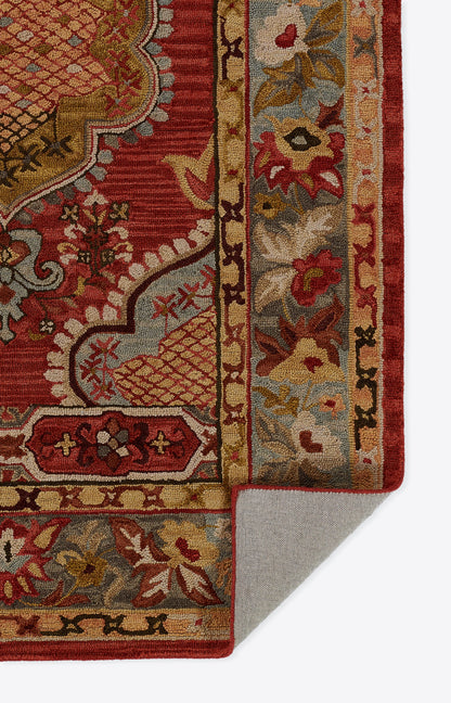 Close-up of red oriental rug edge with gold/cream floral border, woven texture, folded corner showing grey underside.