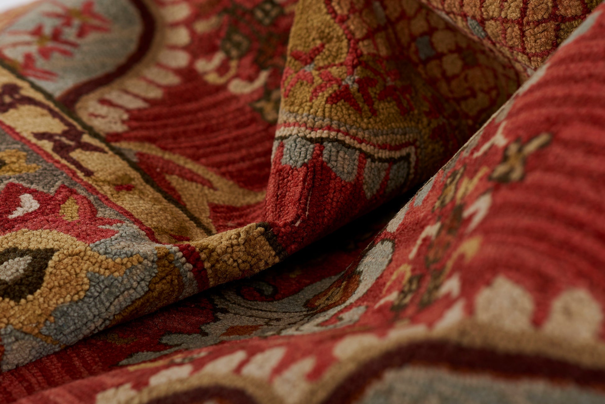 Close-up of a plush red & gold patterned textile with blue and beige accents and curling edge.