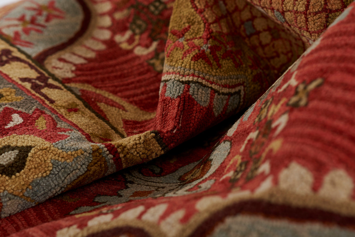Close-up of a red oriental rug with gold, beige and blue patterns; thick wool pile and folded edge.
