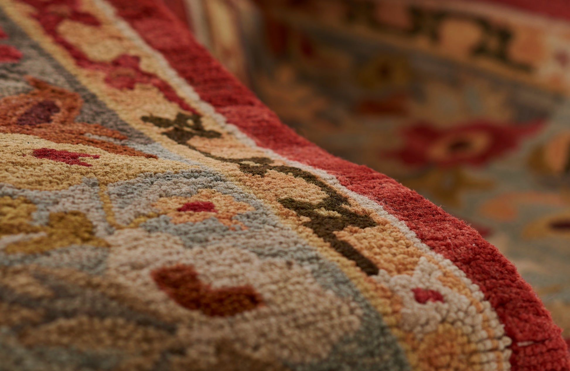 Close-up of a red-bordered oriental rug with beige, blue and gold floral motifs and plush pile.