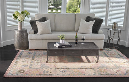 Beige sofa with light and dark cushions, dark metal coffee table on casters, pastel floral rug, wine bottle, glass and plant.