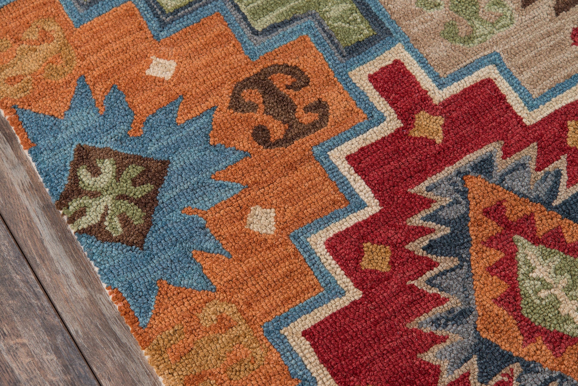 Kilim-style geometric woven rug in orange, blue, red, green with zigzag borders; wood floor visible at edge.