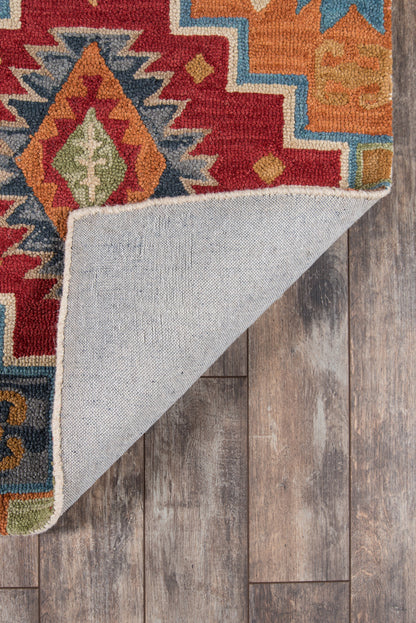 Colorful geometric rug with red, orange, blue, and green motifs; folded corner shows light backing on wood floor.