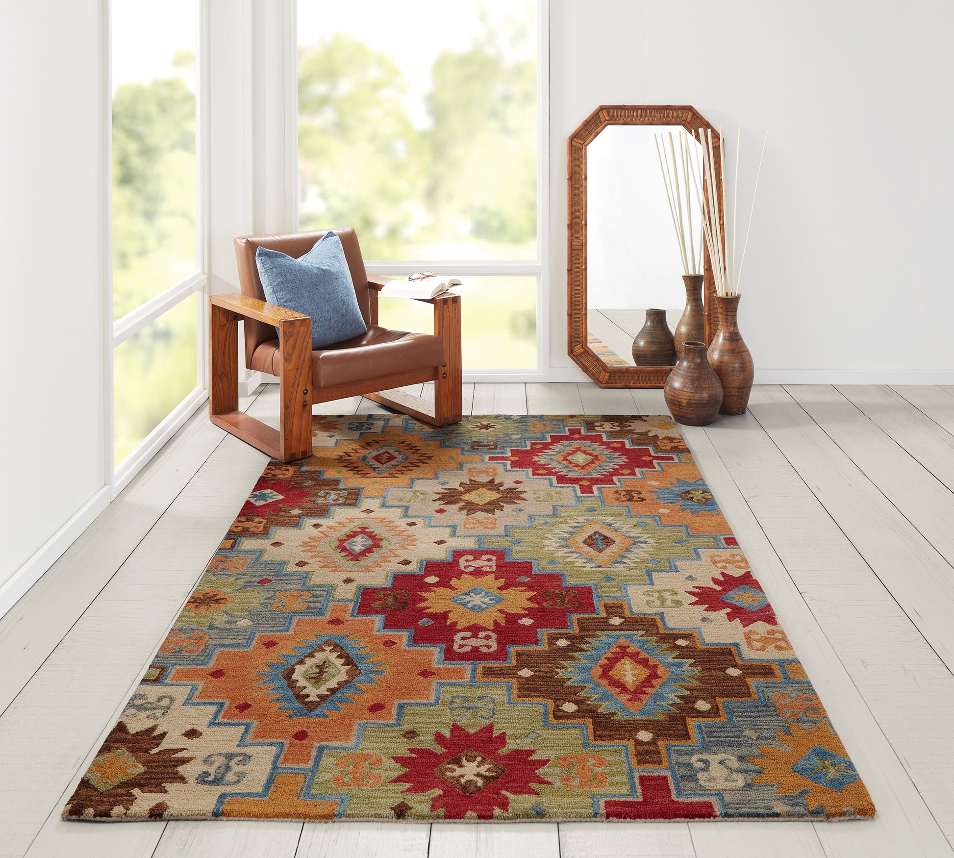 Rectangular Southwestern geometric area rug in red, teal, brown and beige; leather armchair with oak frame, tall wooden-framed mirror and vases.