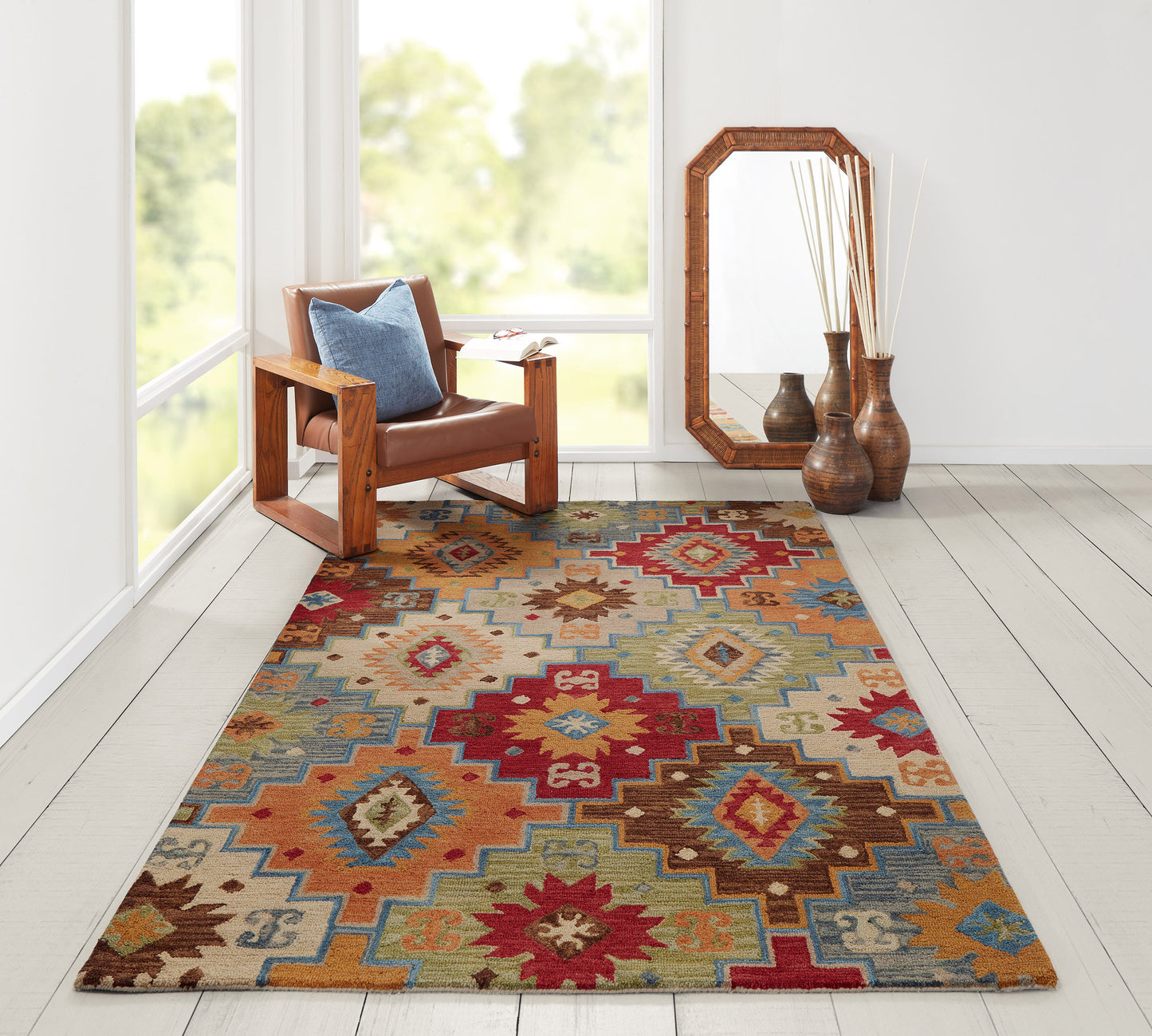 Bold kilim rug in red, teal, and orange tones, on a bright room with a brown leather armchair and wooden mirror.
