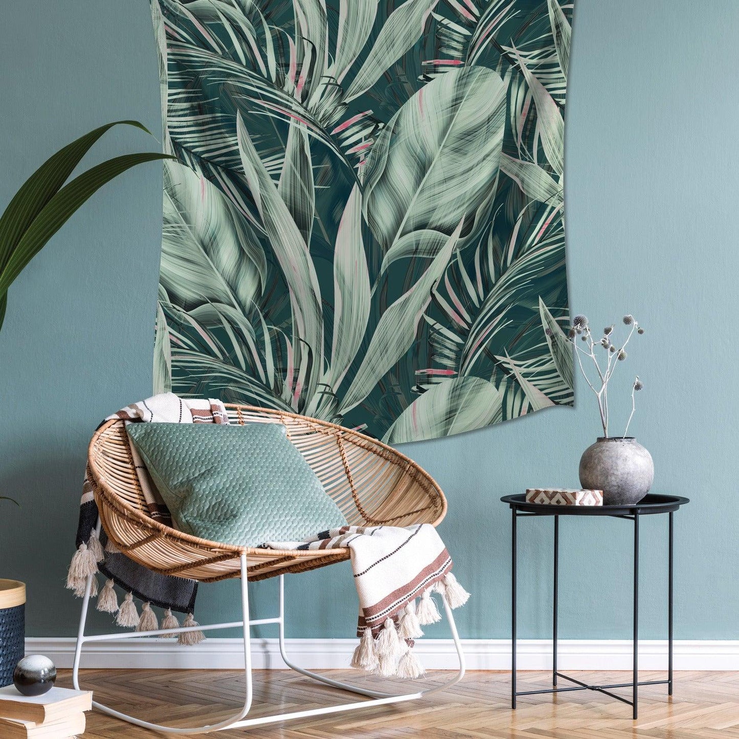 Boho tropical living room with a rattan chair, mint cushion, tasselled throw, leaf wall tapestry, and black metal side table.