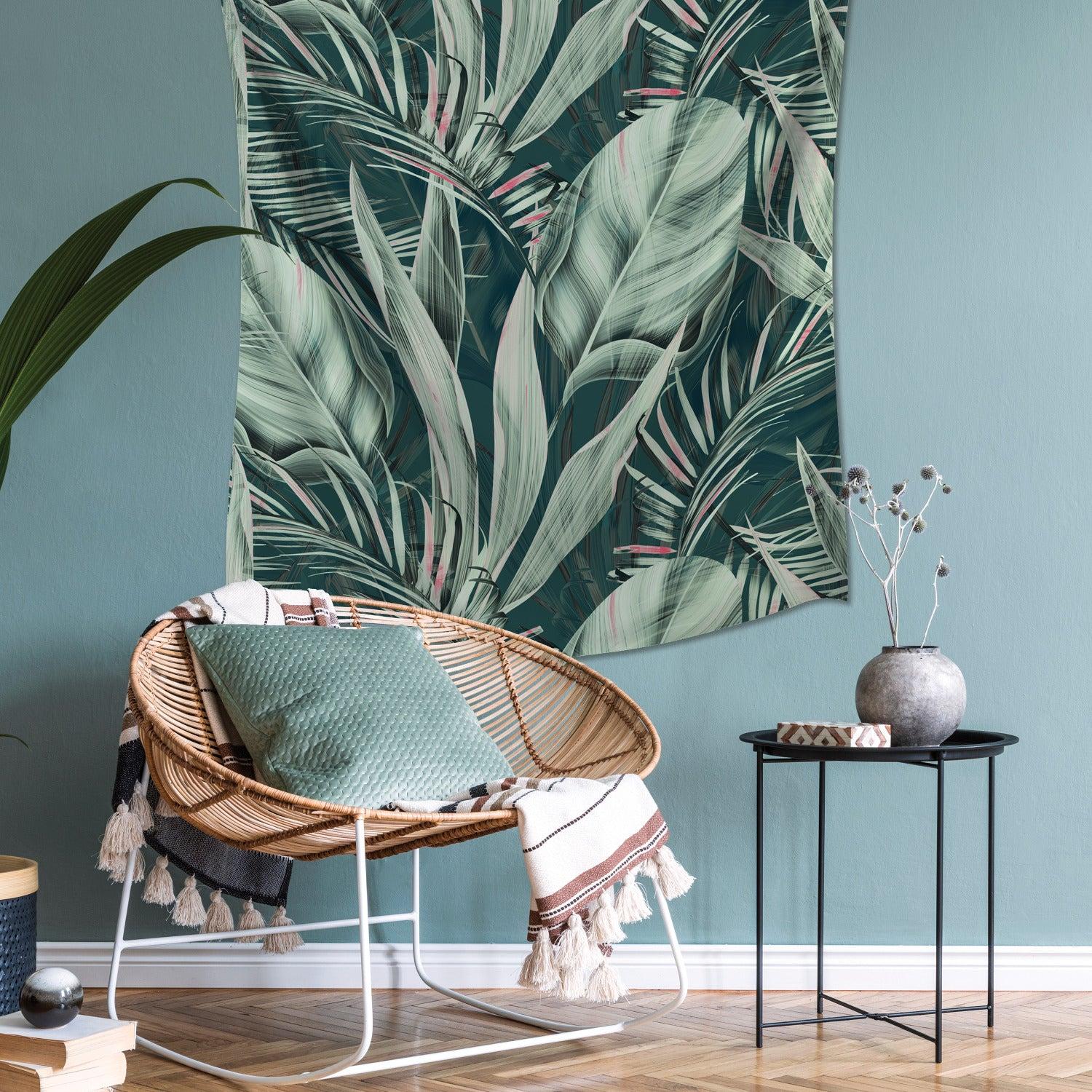 Boho tropical living room with a rattan chair, mint cushion, tasselled throw, leaf wall tapestry, and black metal side table.