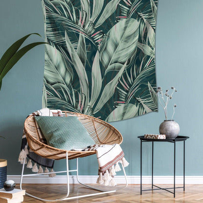 Boho tropical living room with a rattan chair, mint cushion, tasselled throw, leaf wall tapestry, and black metal side table.