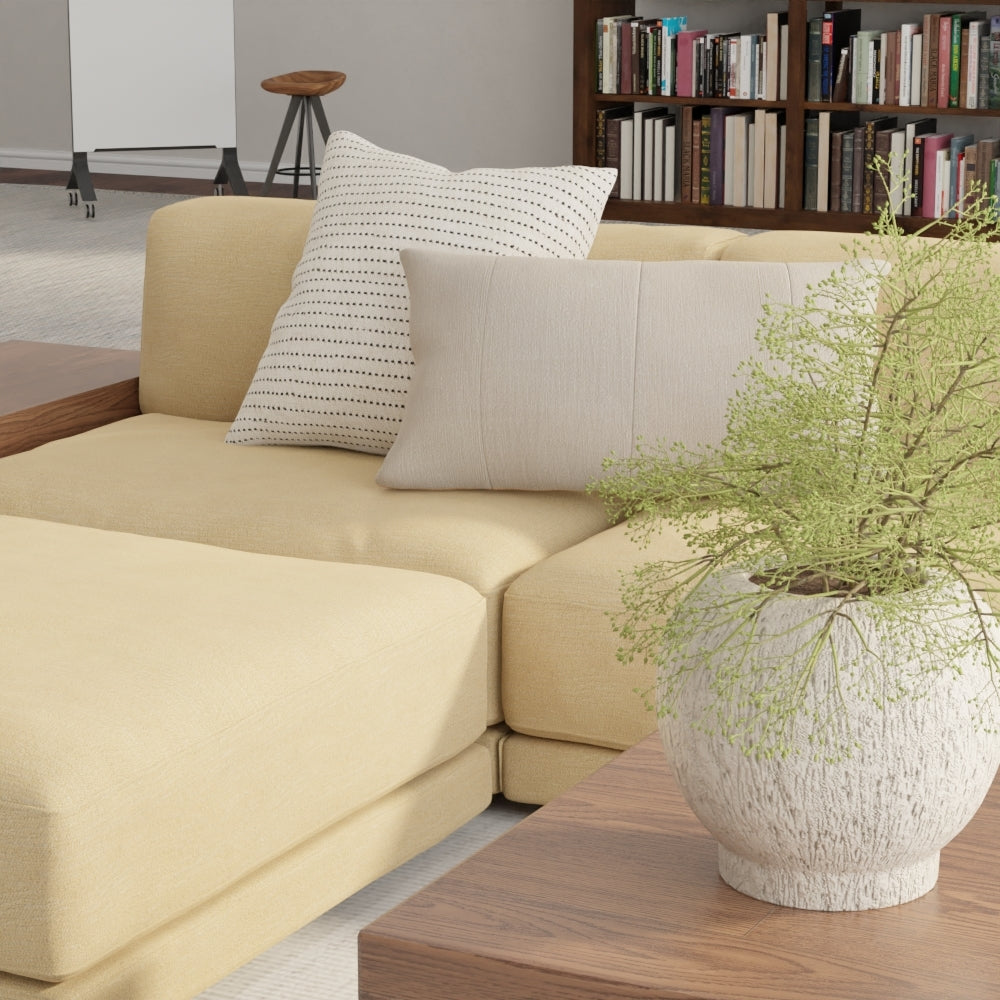 Camel solid fabric sectional sofa with cream cushions and dotted throw pillows, wooden coffee table, greenery planter in a modern living room.