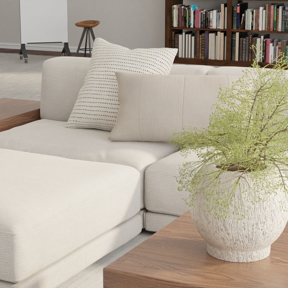 Beige modular sofa upholstered in Mercury solid fabric with dotted cushions, wooden side table, and a ceramic planter with greenery.