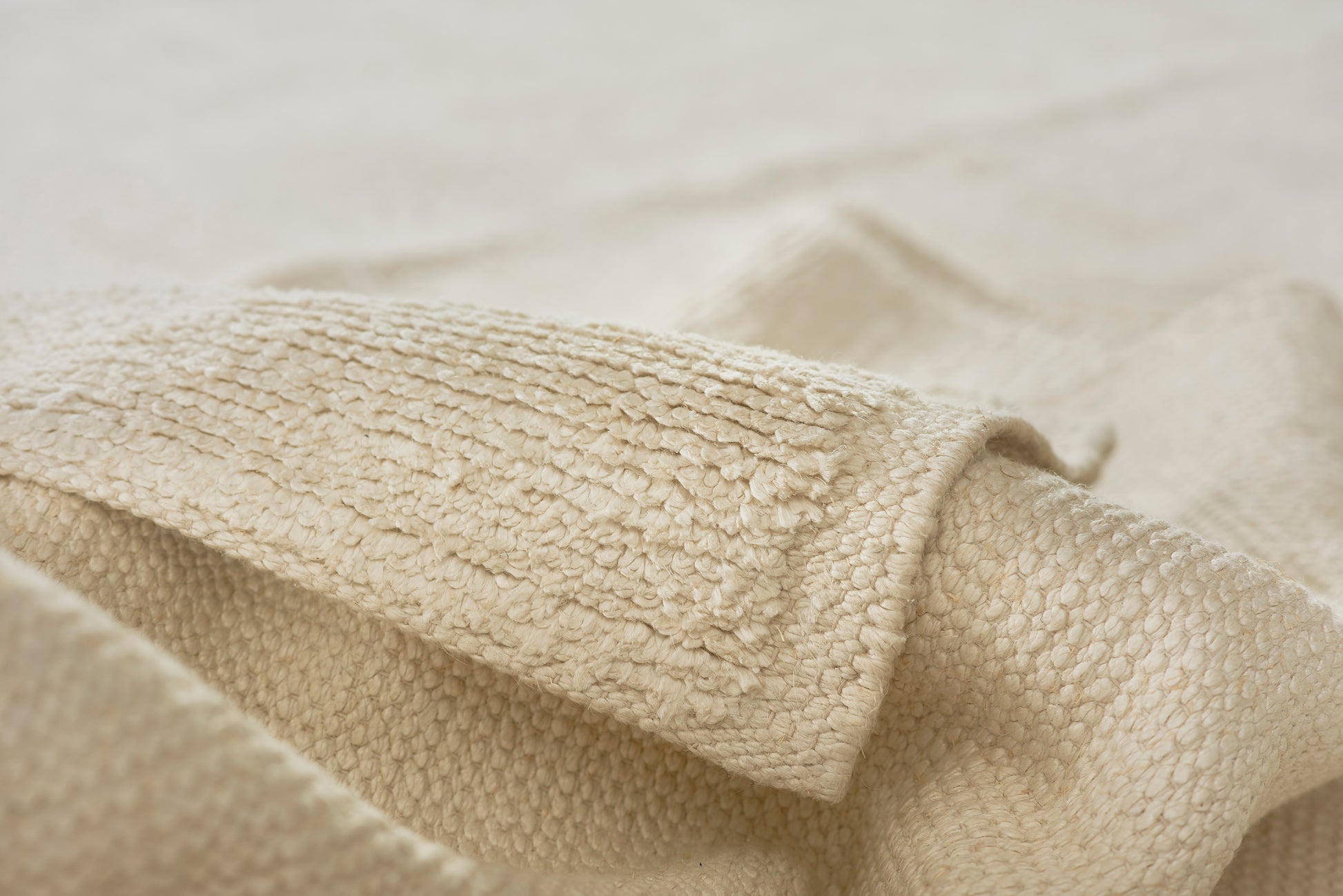 Ivory sherpa fleece with plush textured surface and rolled edge, cozy fabric for blankets or jackets.