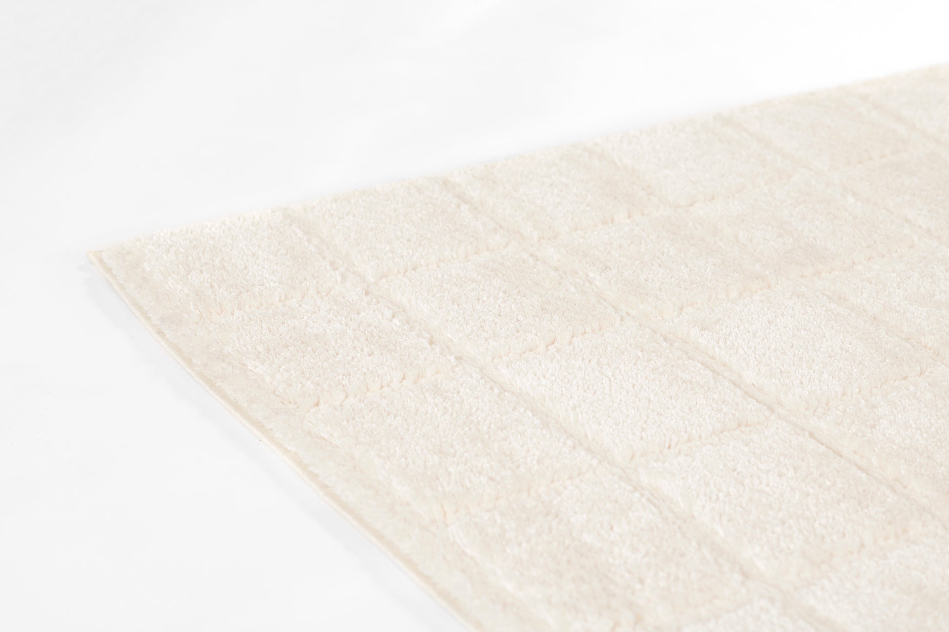 Ivory rectangular rug with plush tufted surface and quilted square pattern.