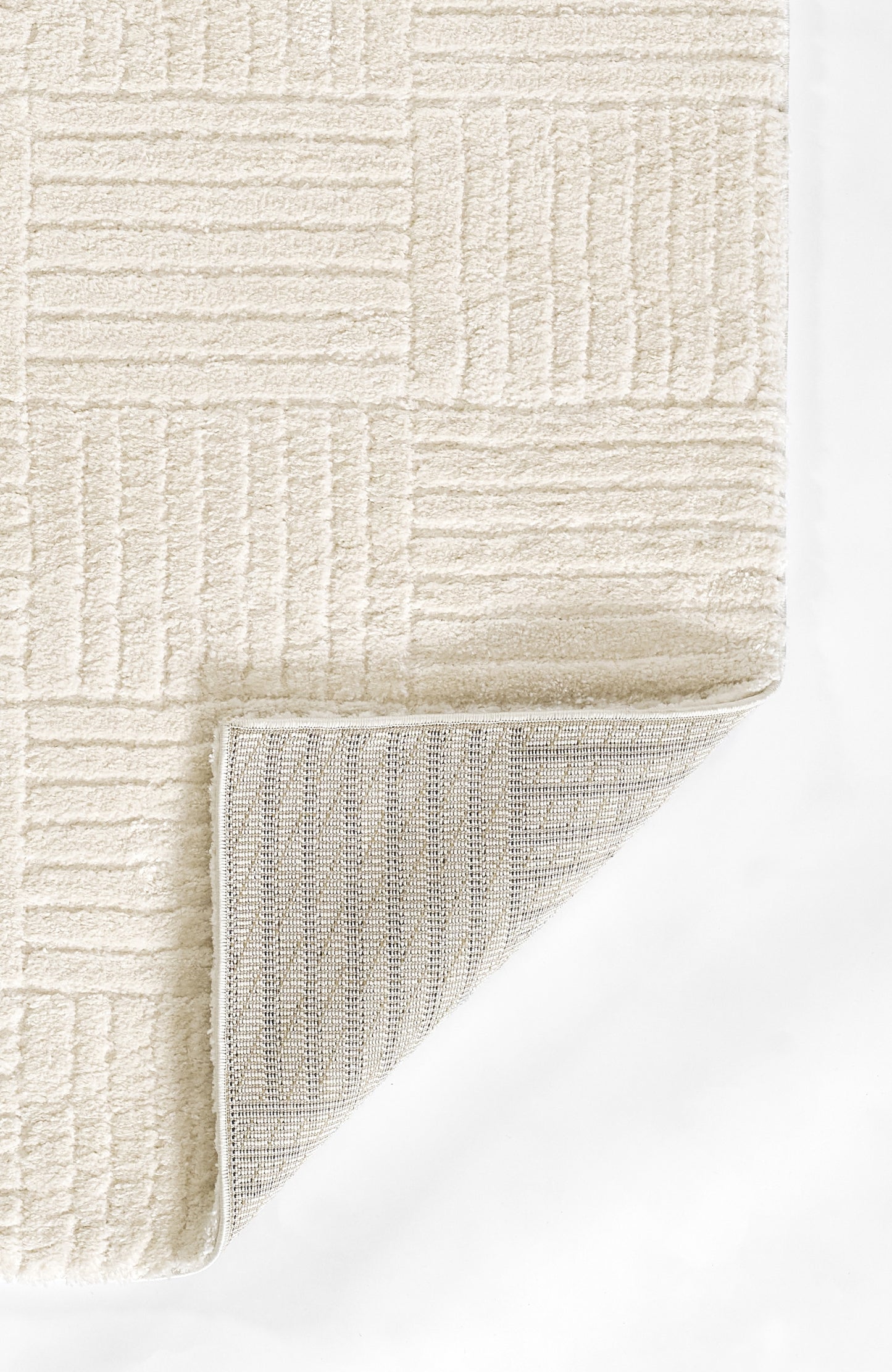 Cream geometric textured rug with plush shag surface and rectangular grid pattern; folded corner reveals grey underside.