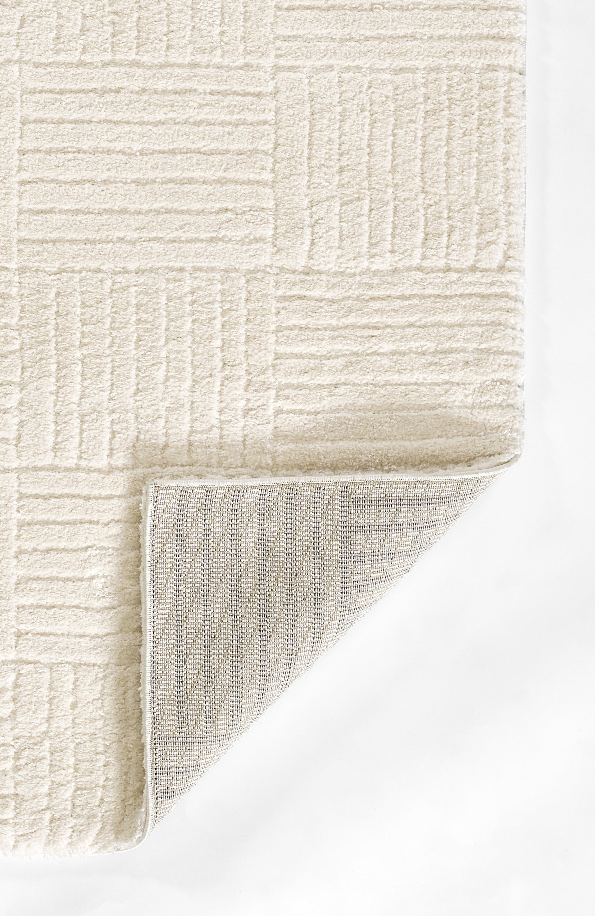 Cream textured area rug with geometric rectangular pattern; folded corner reveals woven beige back.
