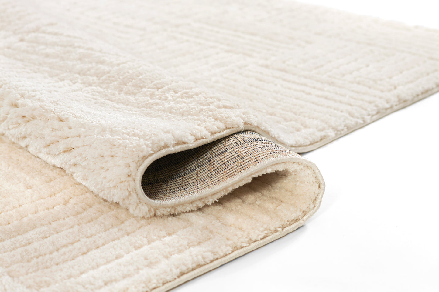 Beige plush shag rug with thick pile, bound edge, rolled to reveal brown woven backing.