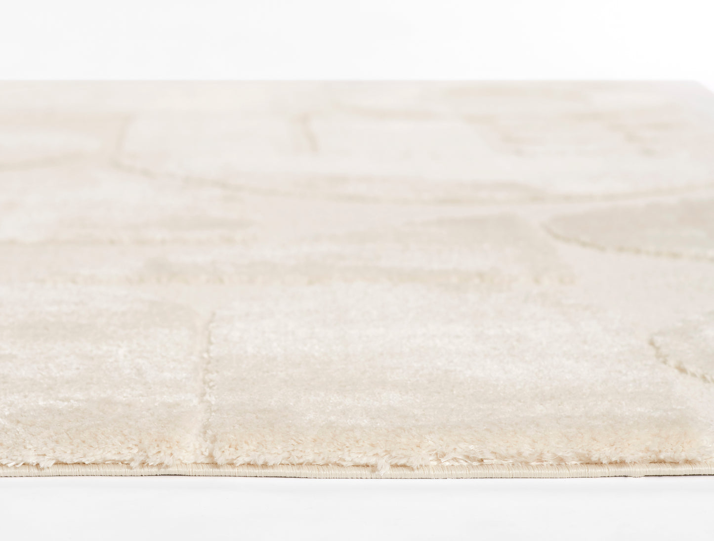 Beige area rug with subtle square patchwork, soft plush pile and fringed edge.