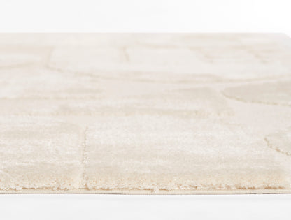 Beige area rug with subtle square patchwork, soft plush pile and fringed edge.