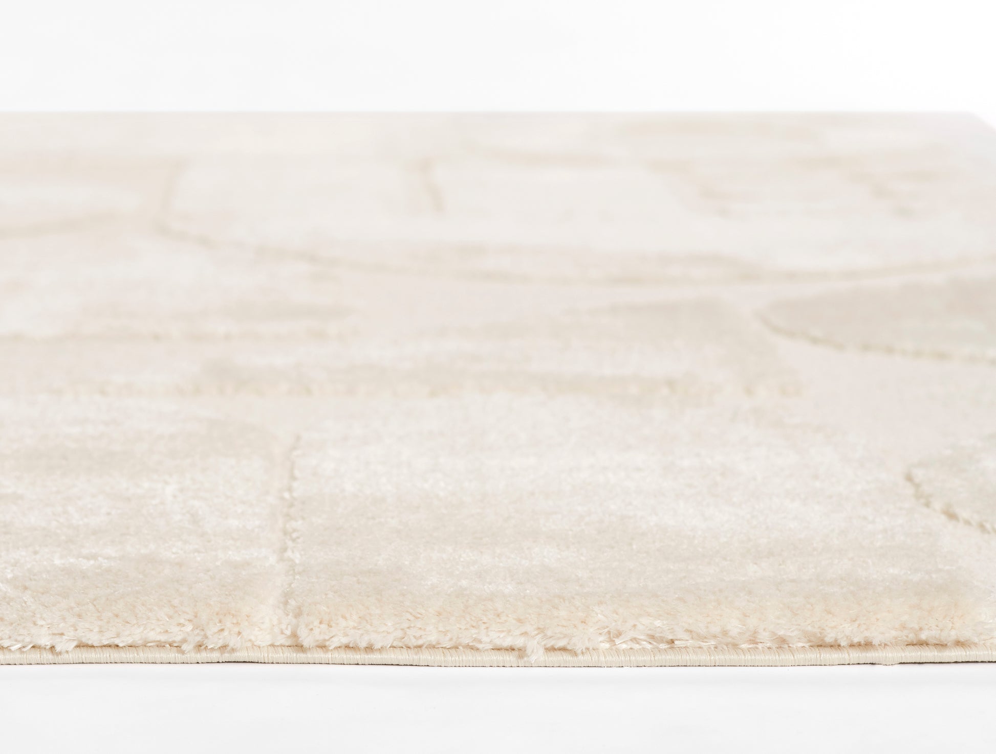 Beige plush area rug with a subtle square grid pattern and fringed edge.