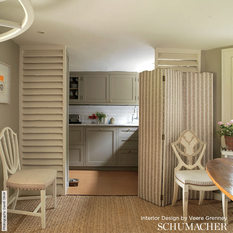Grey shaker kitchen behind a beige patterned folding screen; white chairs, round wood table edge, neutral woven rug.