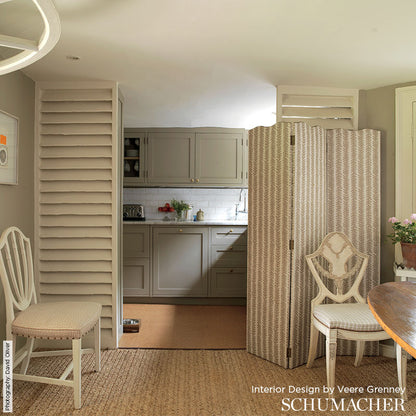 Grey shaker kitchen behind a beige patterned folding screen; white chairs, round wood table edge, neutral woven rug.