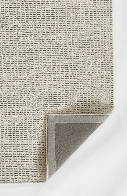 Beige woven area rug with subtle texture & folded corner revealing light gray backing; neutral modern decor.