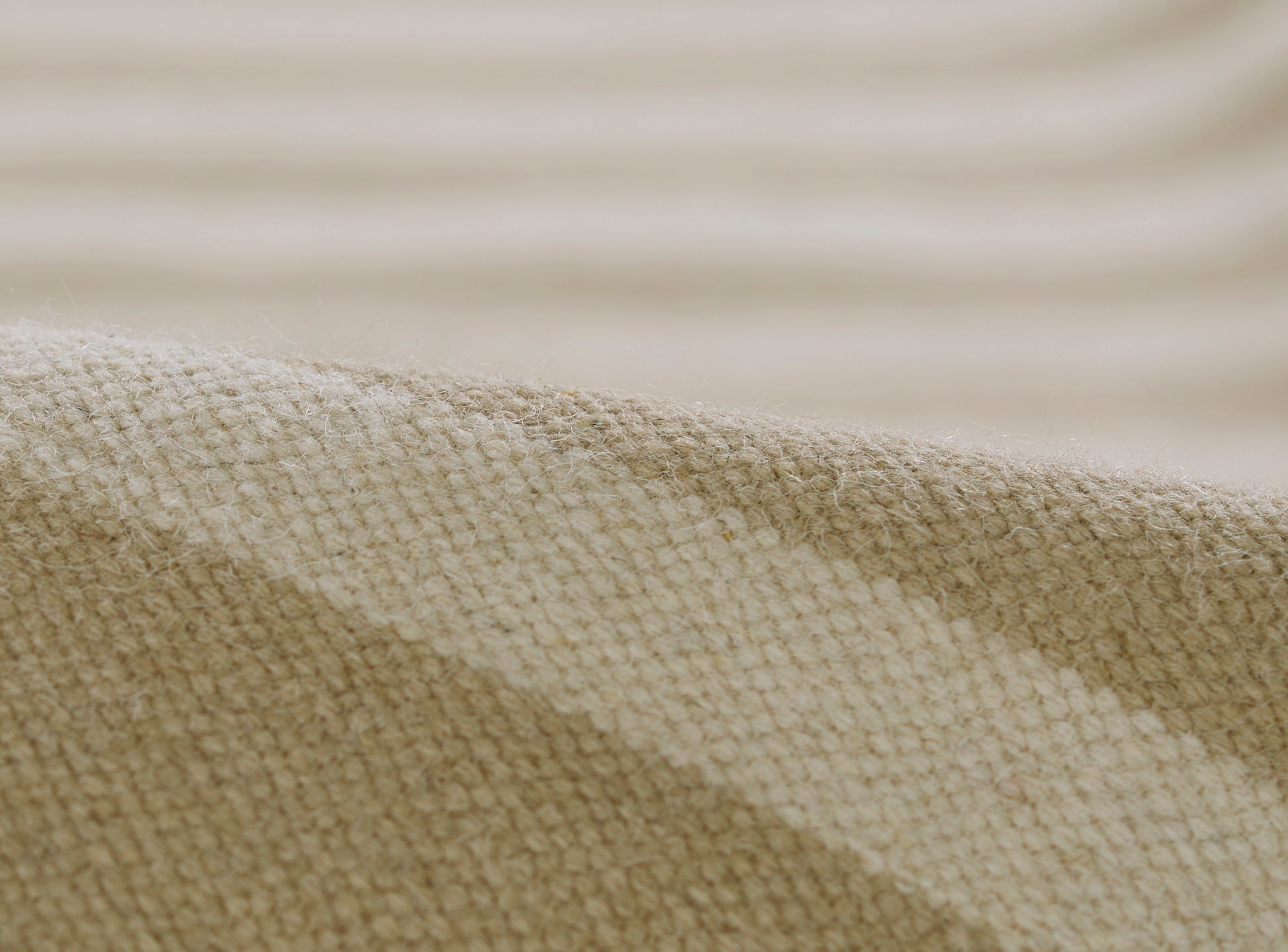 Beige woven rug close-up with a textured surface and soft folds, linen-like material.