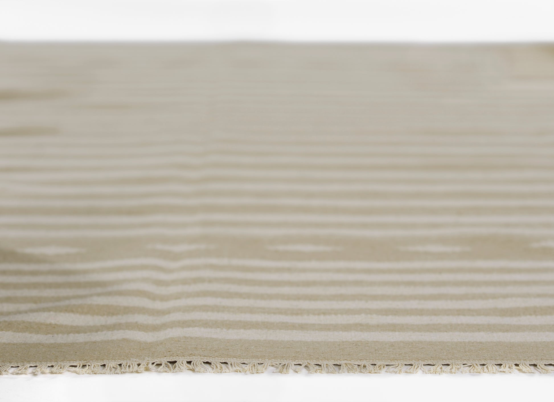 Beige flat-weave rug close-up with subtle horizontal stripes and fringed edge.