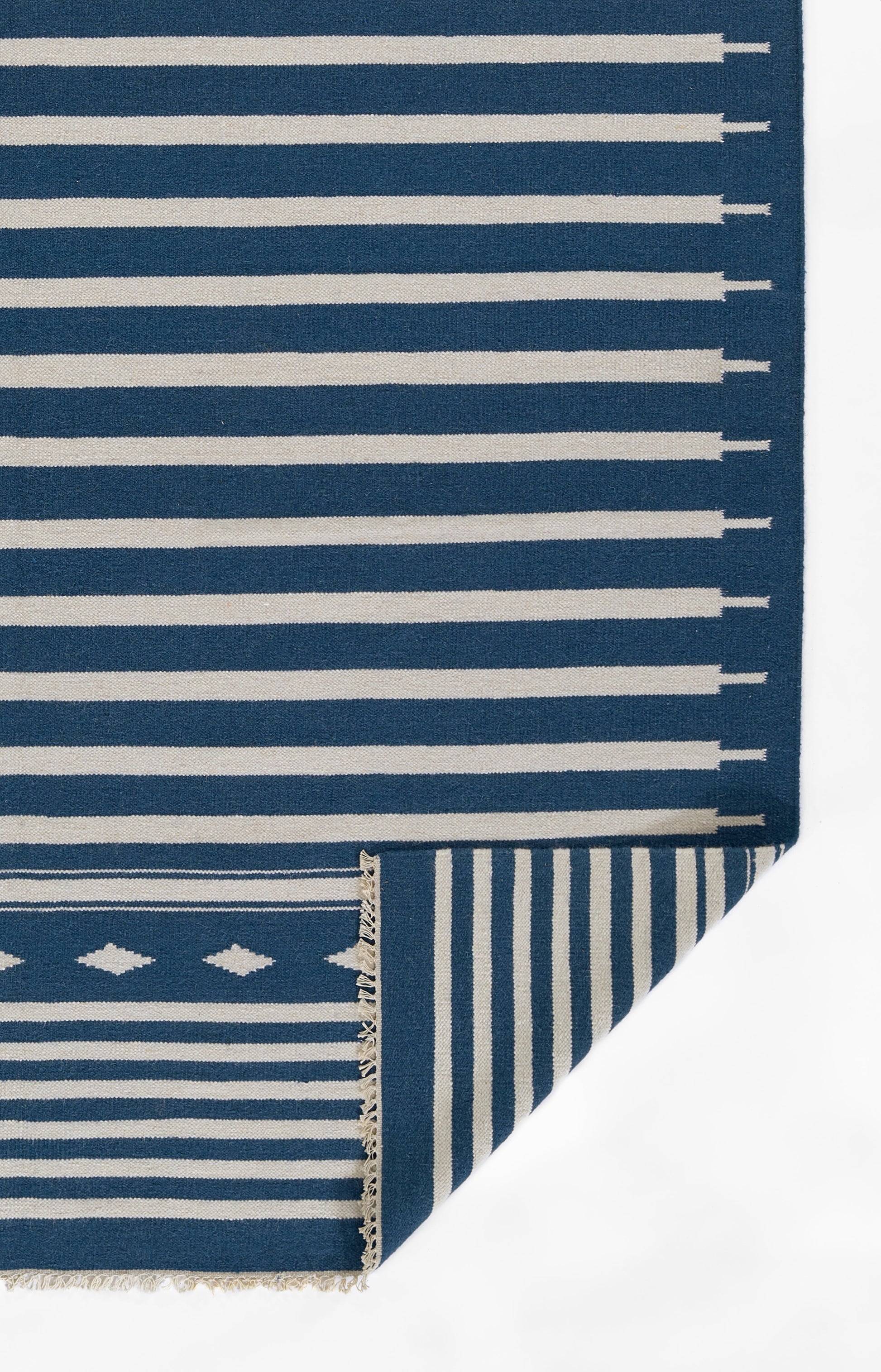 Blue and white striped woven rug with folded corner showing reverse stripe pattern and fringe.