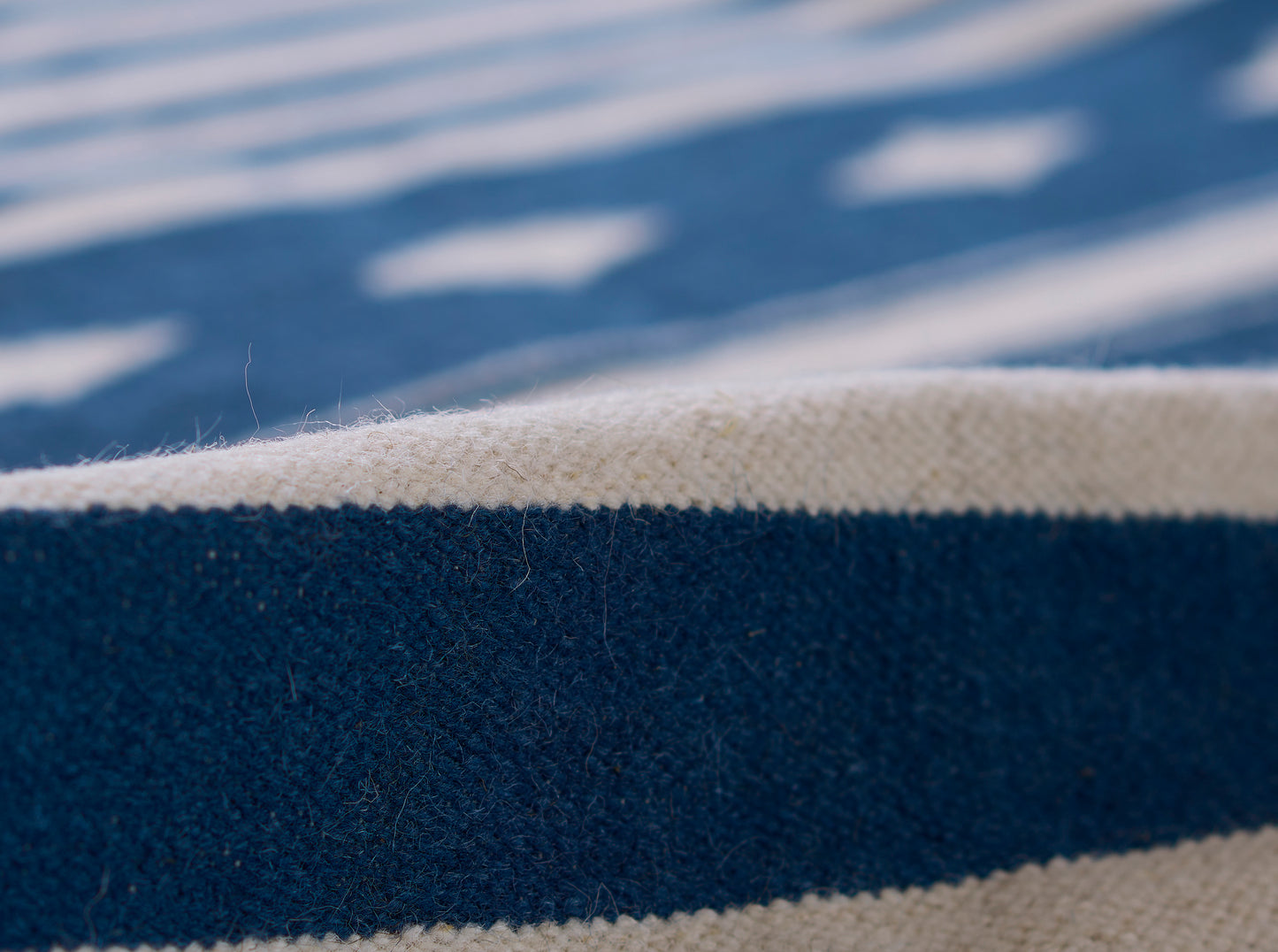 Close-up of navy blue stripe on beige woven rug; soft, chunky textile with nautical striped design.
